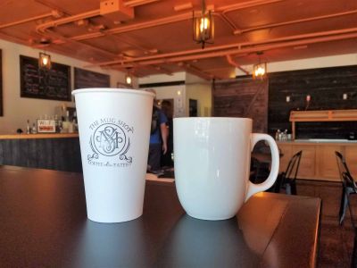 Shop logo on paper cup and mug at The Mug Shot Coffee & Eatery
