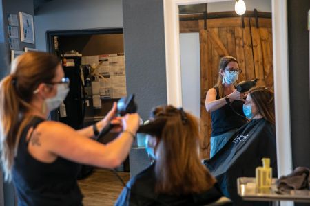 a hairdresser dries a client's hair while wearing a mask